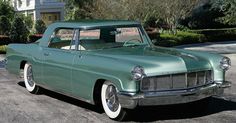 an old green car parked in front of a house