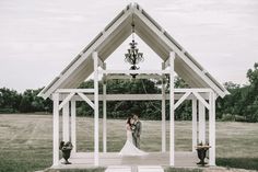 a bride and groom standing in front of a white gazebo with chandelier