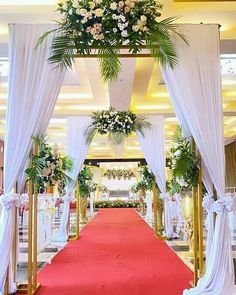 a red carpeted aisle with white drapes and flowers on the top is decorated for a wedding