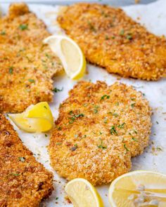 three pieces of chicken with lemons and parmesan cheese on the side next to some sliced lemons