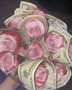 a bouquet of pink roses sitting on top of one hundred dollar bills in someone's hand