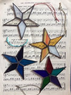 four stained glass star ornaments on sheet music paper with string attached to them, all in different shapes and sizes