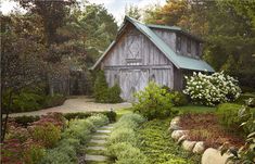 an old barn sits in the middle of a garden with stone steps leading up to it