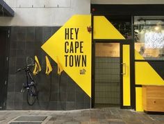 a yellow sign that says hey cape town on the side of a building with a bike leaning against it