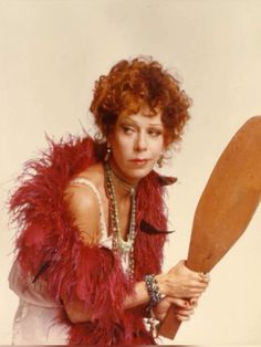 a woman holding a large wooden spatula in her right hand and wearing a red feather boa