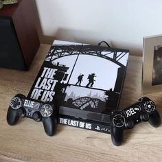 two video game controllers sitting on top of a wooden table next to a box with the last of us