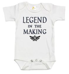 Rapunzie's adorable baby onesie, perfect for little ones who are destined to become legends! Made from 100% cotton, this short-sleeve onesie ensures utmost comfort for your precious bundle of joy. With its charming design featuring the iconic Legend of Zelda video game symbol and the captivating caption, "Legend in the Making," your baby will surely make a statement wherever they go.Crafted with love and attention to detail, this baby onesie combines style and softness to create a delightful out Cotton Short Sleeve Bodysuit With Character Print, Cotton Bodysuit With Character Print And Short Sleeves, Short Sleeve Onesie For Father's Day Gift, Pre-shrunk Short Sleeve Onesie For Playtime, White Short Sleeve Onesie With Character Print, Customizable Cotton Onesie For Father's Day, Cotton Onesie For Father's Day, Funny Customizable Short Sleeve Onesie, Unisex Short Sleeve Onesie As Gift