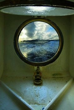 a porthole window on the side of a ship looking out at the ocean and clouds