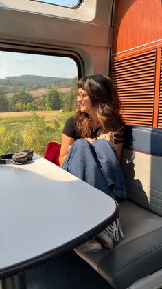 a woman sitting at a table looking out the window on a train with mountains in the background