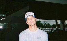 a man wearing a baseball cap standing in front of a window with cars behind him