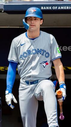 a baseball player sitting in the dugout with his glove on and holding a bat