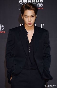 the young man is wearing a black suit and posing in front of a red carpet