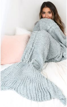 a woman laying on top of a bed covered in a mermaid tail knitted blanket