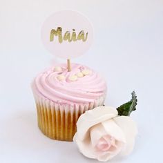 a cupcake with pink frosting and a white rose next to it that says mia