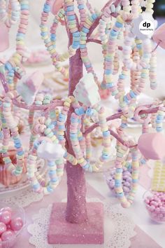 a pink and white table topped with lots of candy covered candies next to a tree