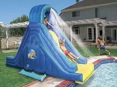 two children are sliding down an inflatable water slide that is on the lawn