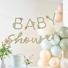 a baby shower banner with flowers and balloons in the background on a cake table at a baby shower