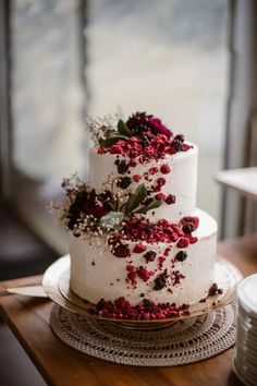 a three tiered white cake with red flowers and greenery on the top layer