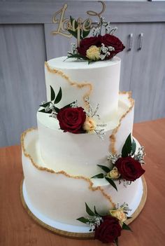 a three tiered wedding cake with red roses and greenery on the top layer