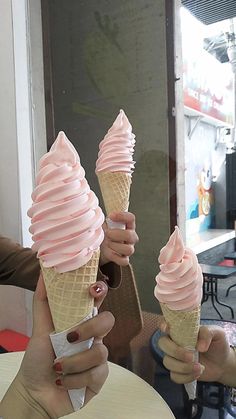 two people holding up ice cream cones in their hands, one has pink icing on it