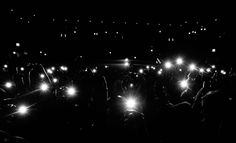 a group of people standing in the dark holding up their cell phones with bright lights shining on them