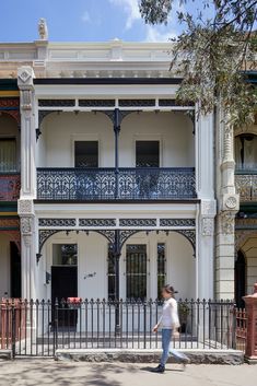 a woman walking down the street in front of a white building with wrought iron railings