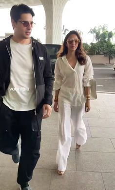 the man and woman are walking together on the sidewalk in front of an airport terminal