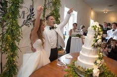 a newly married couple standing in front of a wedding cake with greenery on it