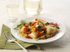 a white plate topped with pasta and veggies next to a glass of water