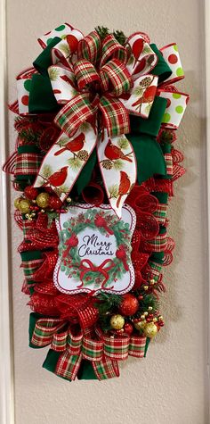 a christmas wreath hanging on the wall with red, green and white ribbon around it