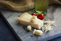 a piece of cheese on a cutting board next to tomatoes and parmesan cheese