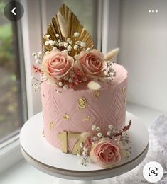 there is a pink cake with gold decorations on the top and flowers on the bottom