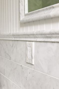 a bathroom with white marble tile and a mirror on the wall, along with a light switch