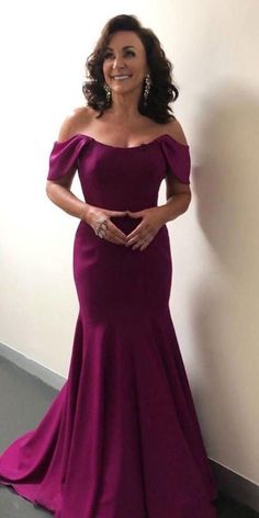 a woman standing next to a wall wearing a purple dress and smiling at the camera