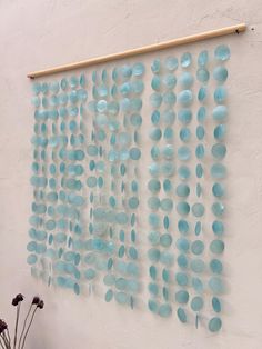 a wall hanging made out of blue glass plates and wood sticks with flowers in front of it