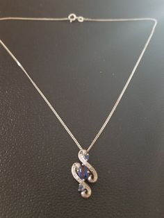 "Sterling silver pendant with blue stones stones and diamond chips. The pendant is a slide and has two s-type swirls. In the center is an oval blue stone and two small and two smaller stones are mounted on top and bottom of the blue stone. The blue stone is a lab created sapphire. Small diamond chips are mounted on the swirls. The slide is marked \"925\". It comes with a 16 inch sterling silver curb chain necklace." Blue Oval Pendant Necklace With Diamond Accents, Blue Stone Necklaces For Anniversary, Silver Figaro Chain Necklace, Figaro Chain Necklace, Curb Chain Necklace, Dog Pendant, Blue Stones, Silver Flats, Moonstone Pendant