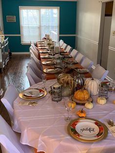 a long table set with plates, silverware and pumpkins