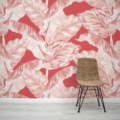 a chair sitting in front of a pink and white wall with large leaves on it