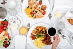 a person holding a coffee cup in front of a table full of breakfast foods and drinks