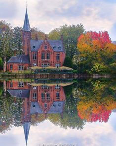 an old red brick building is reflected in the still waters of a lake surrounded by trees