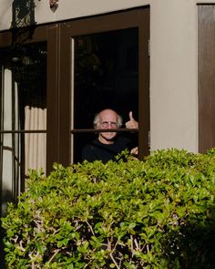 an older man is looking out the window with his thumb up in front of him