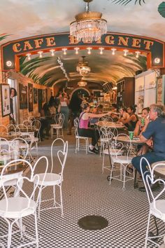 people are sitting at tables in an old fashioned restaurant with chandeliers hanging from the ceiling