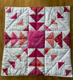 a pink and white quilted table topper on a wooden surface with an arrow design