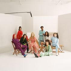 a group of women sitting next to each other on chairs in front of a white wall