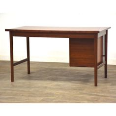 a wooden desk sitting on top of a hard wood floor next to a white wall