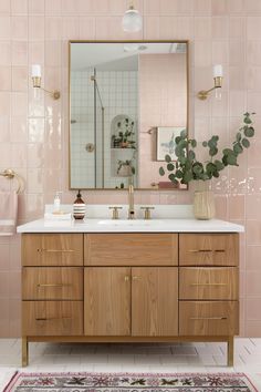 a bathroom with pink tiles and wooden cabinets, gold faucet, white counter top