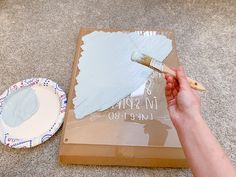 someone is painting the bottom of a cardboard box with white paint and a wooden brush