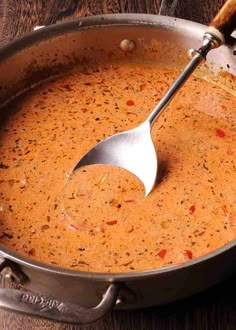 a large pot filled with soup on top of a wooden table next to a spoon