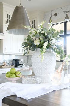 a white vase filled with flowers sitting on top of a kitchen counter next to green apples