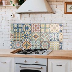 a stove top oven sitting inside of a kitchen next to a white brick wall with colorful tiles on it